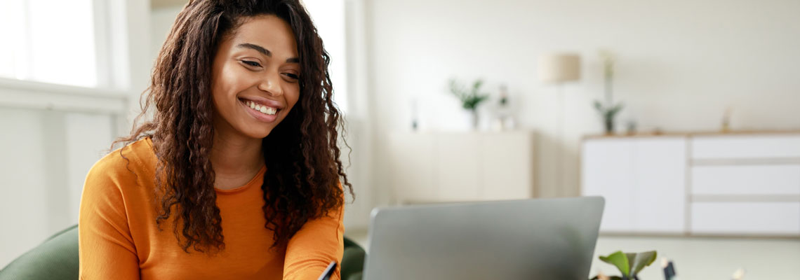 Smiling young woman sitting at desk working on laptop