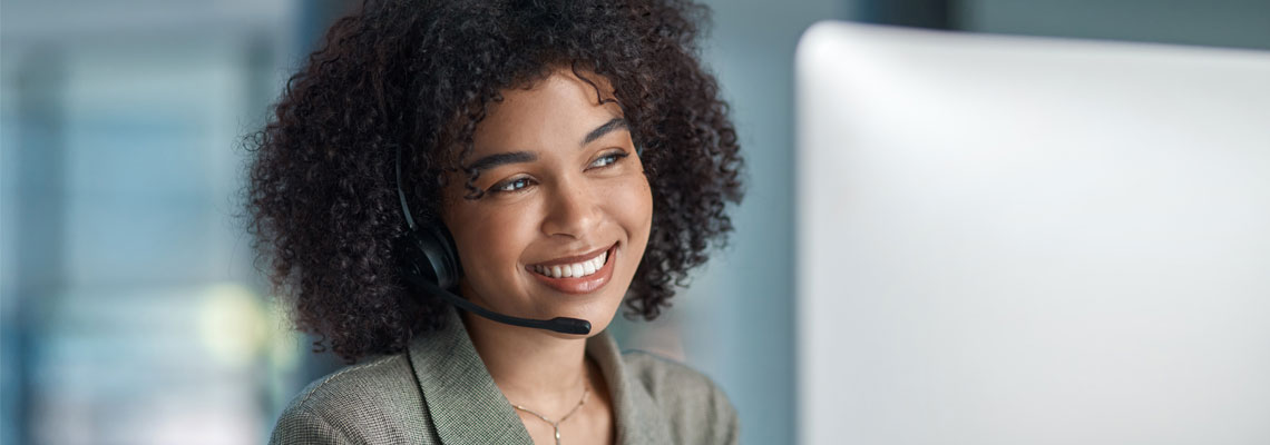 Smiling customer service agent wearing a headset and using a computer in an office