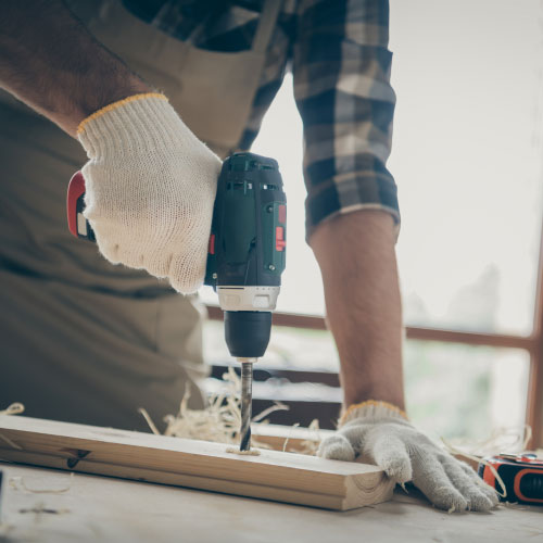 man drilling wood equipped with gloves doing his work indoors