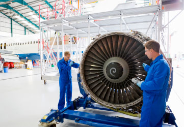 Engineers in uniforms assembling the turbine engine of a passenger jet at a hangar.