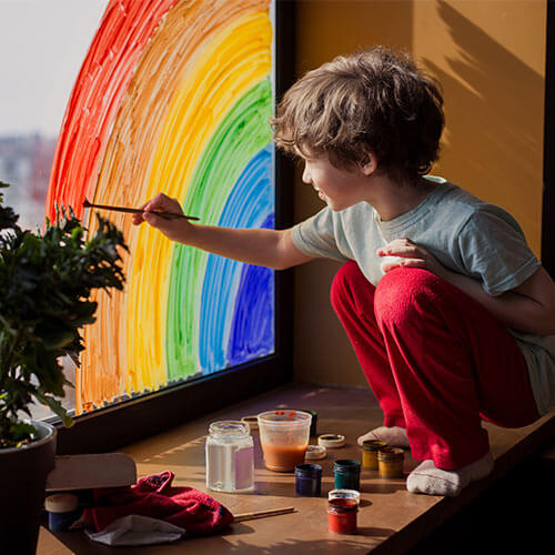Child painting a rainbow on a window