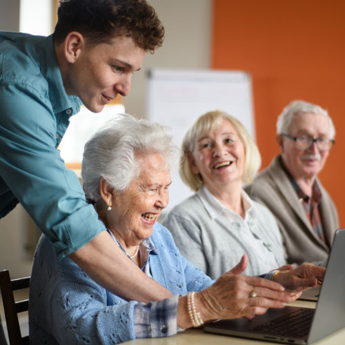 Senior group in retirement home with young instructor learning in computer class