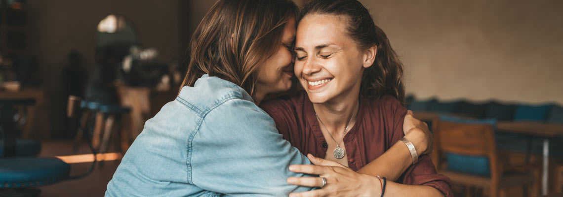 Happy young woman hugging her best friend, sitting in a café