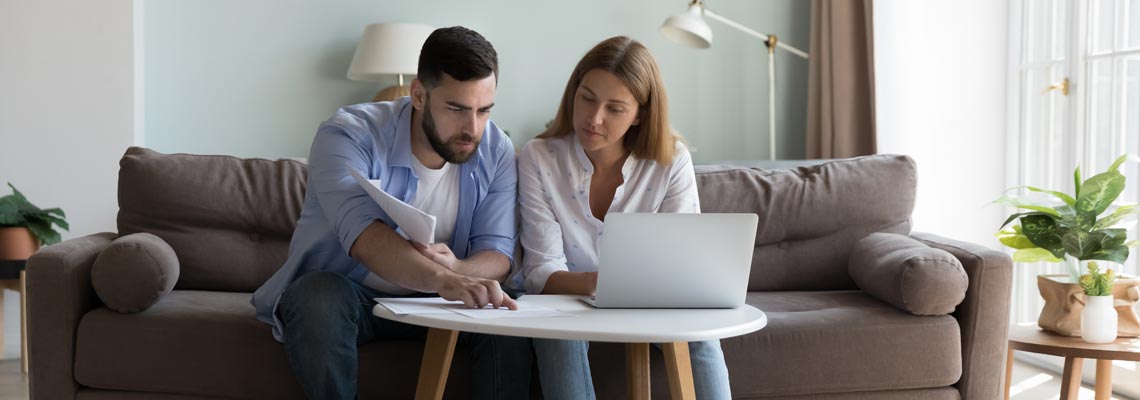 couple sit on sofa reviewing bills