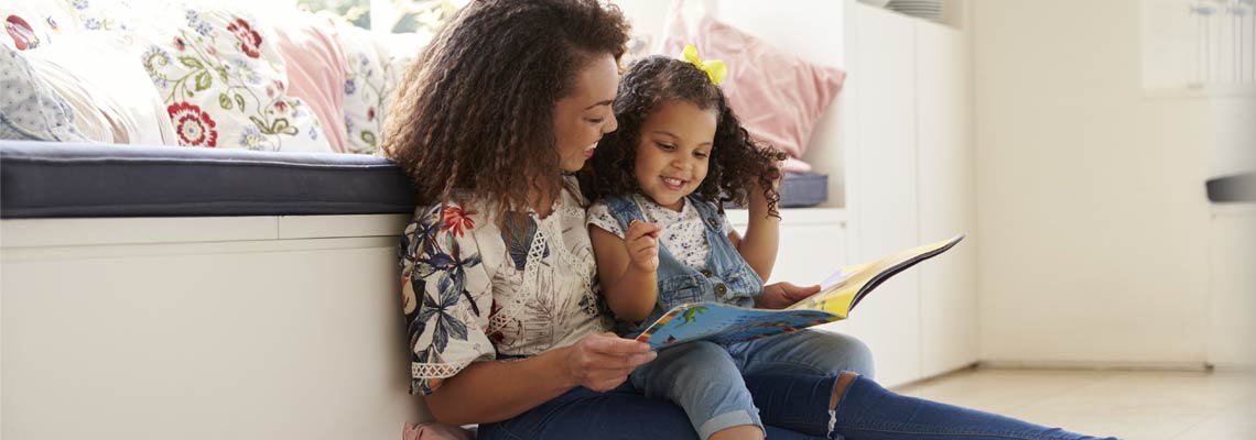 Mother sitting on the floor reading a book with her daughter