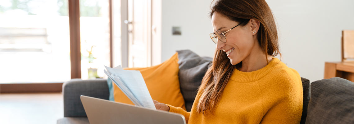 woman wearing yellow jumper sitting on sofa with laptop and papers