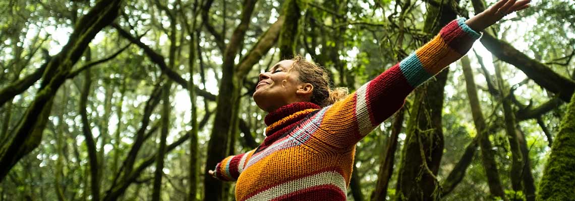 Ground view of joyful woman with arms up standing in the deep forest