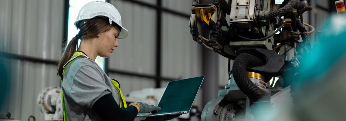 Female engineer using laptop checking automation of robot arms machine