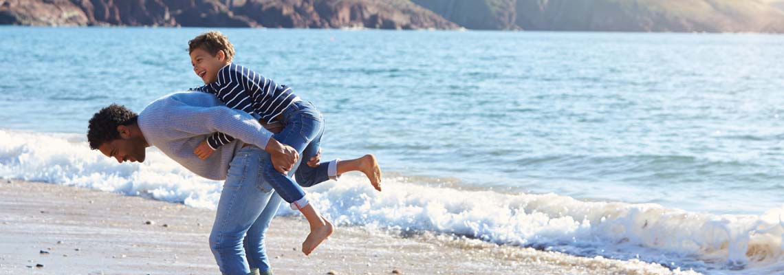 Father giving son piggyback as they walk along the beach
