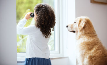young girl looking through the window with her dog sitting beside her