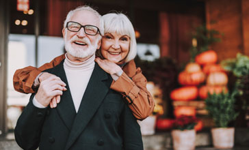 mature woman hugging husband from behind while he is holding her hand