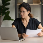 woman looking at laptop while holding documents