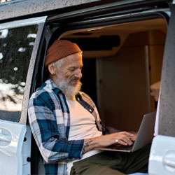 Happy older man sitting in rv camper van using laptop