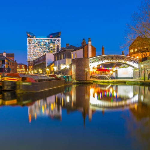The cube behind brick buildings alongside a water channel in the central Birmingham