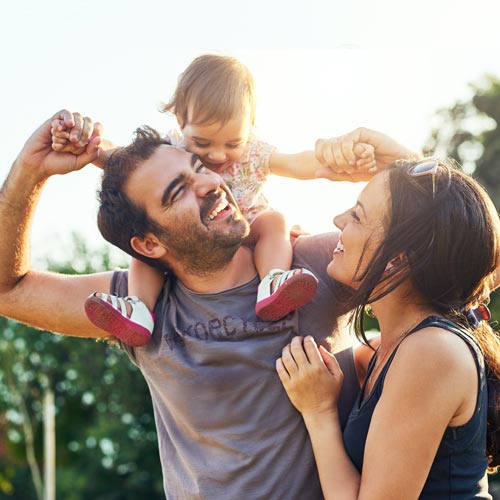 Daughter sitting on father's shoulders in park with mom