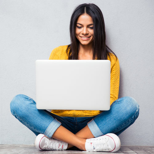 Happy young woman sitting on the floor and using laptop