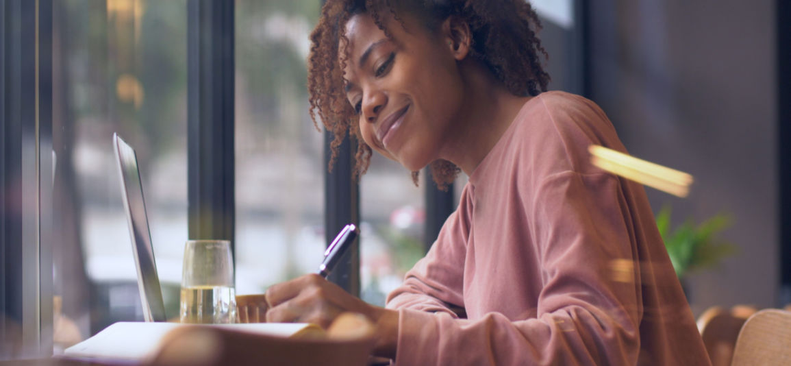 Young black woman writing a letter next to her laptop