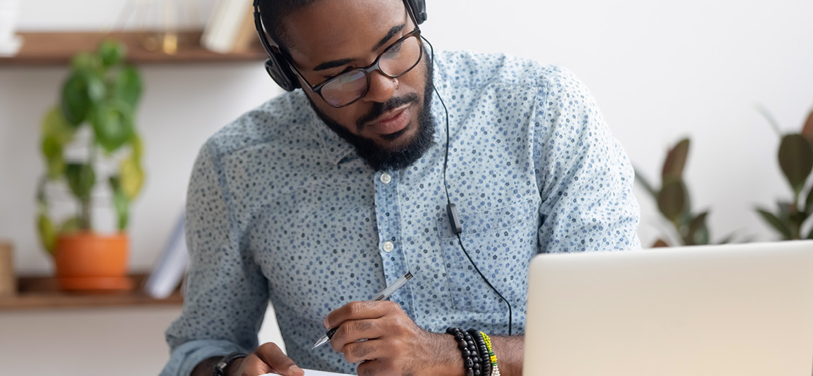 man wearing headphones and taking notes on laptop
