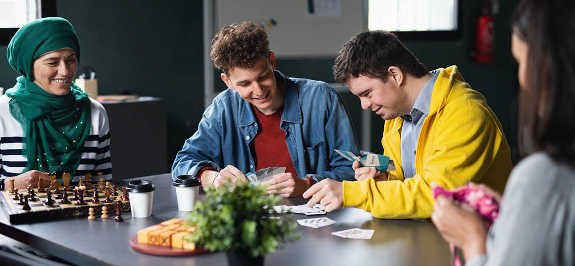 2 people at a desk in a community centre playing a card game