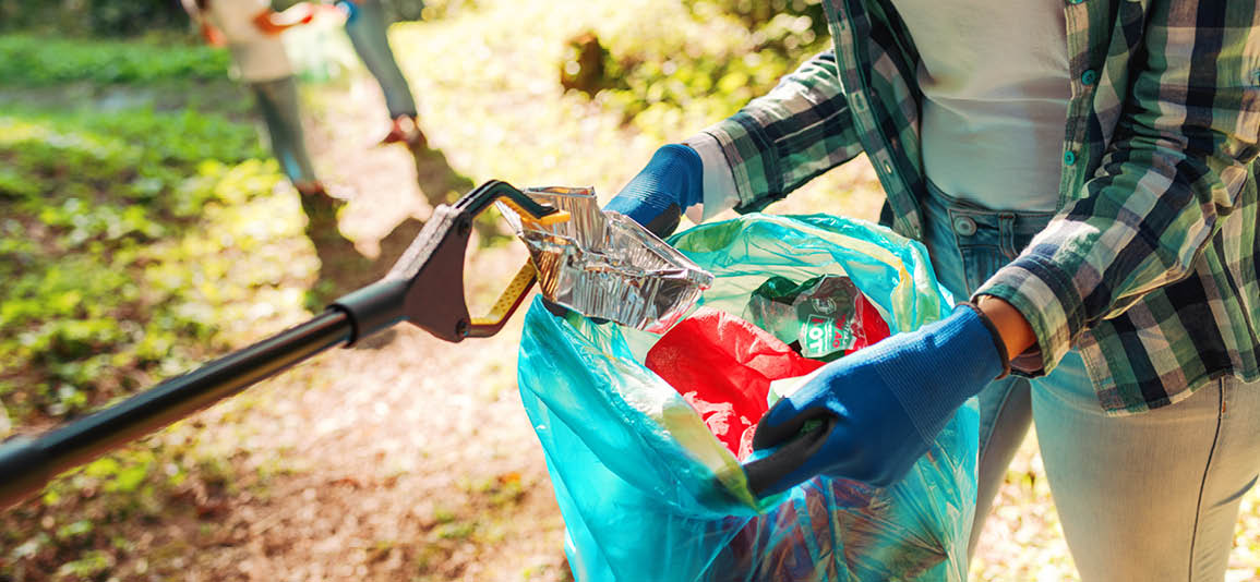 A close up image of a litter picking device clutching waste with a volunteer holding open a rubbish bag to drop the waste into.