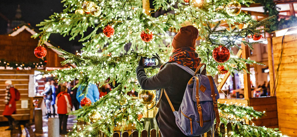 Image of a person taking a selfie in front of a Christmas tree in a town market