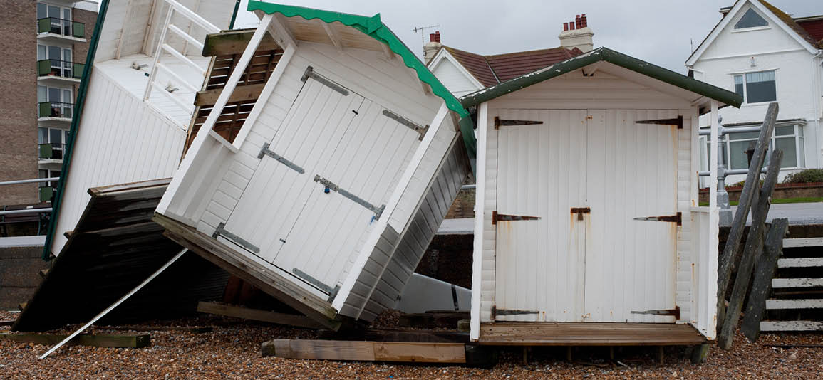 Beach huts have suffered damage from high winds during a storm. Huts have been blown over on their sides at various angles standing on a pebble beach