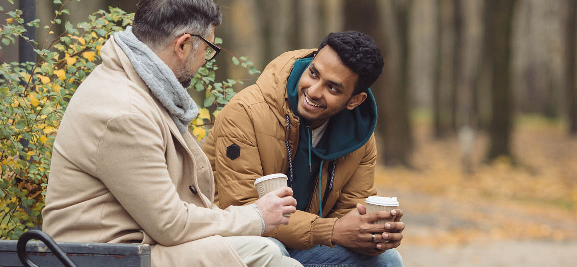 2 people on a bench talking while holding coffee
