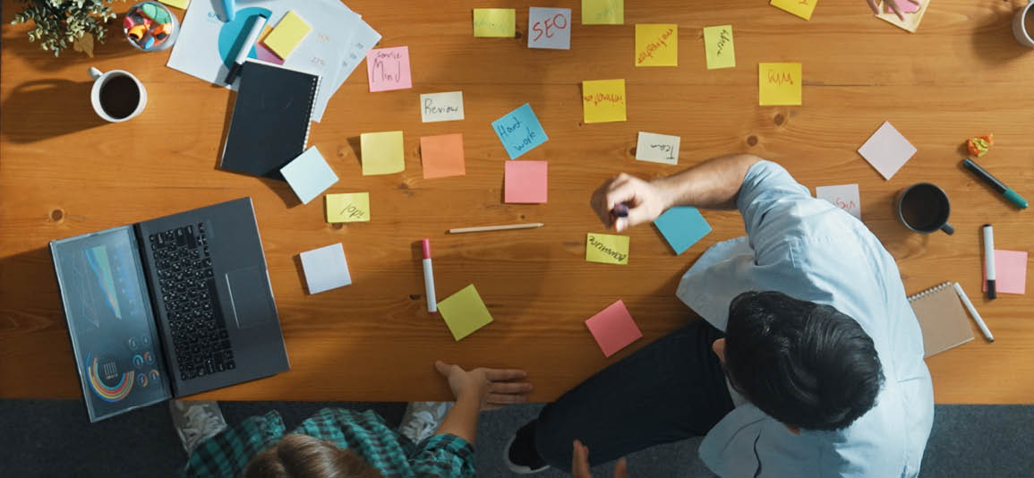 High view image of group of people working on a plan with a desk of sticky notes and a laptop