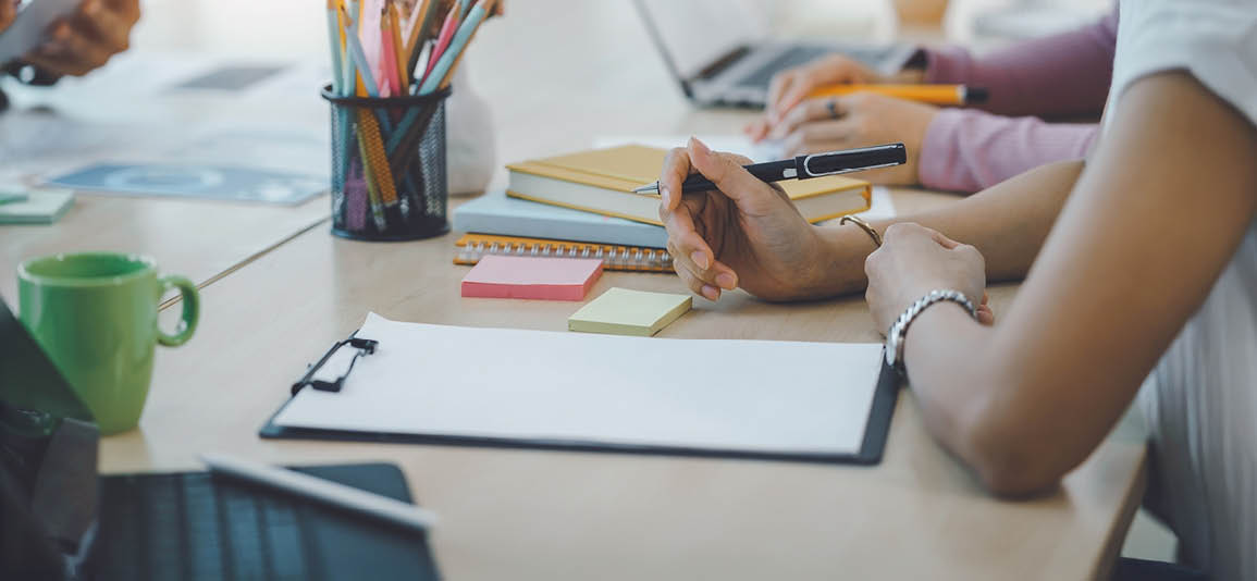 Close-up of office desk with notebooks, sticky notes, pencils, and laptops during a planning meeting