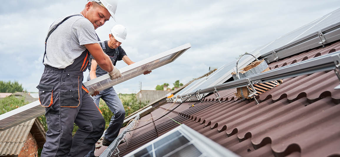 Two men in hardhats installing solar panel on roof