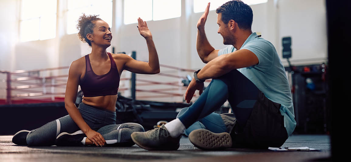 2 people about to high 5 while sitting on the gym floor after completed a workout