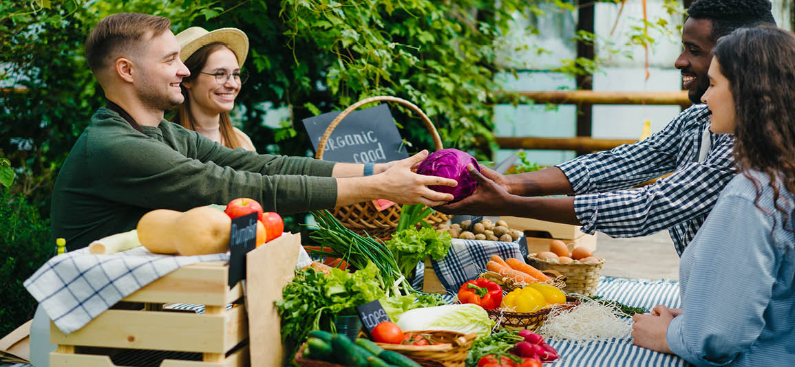 Man and women selling fruit and veg in their garden to a couple