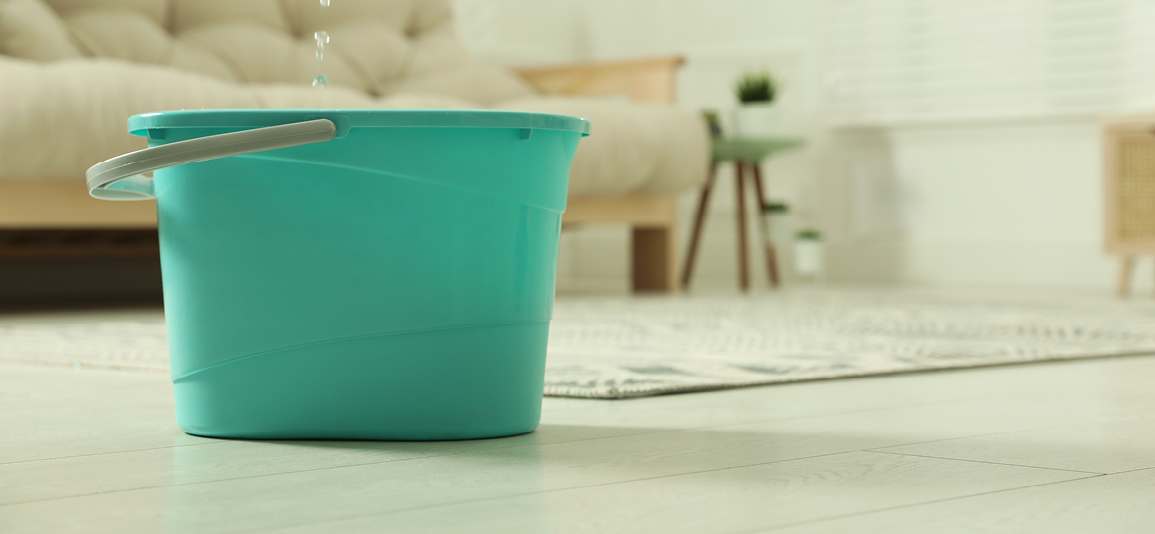 bucket in a living room collecting leaks from a ceiling