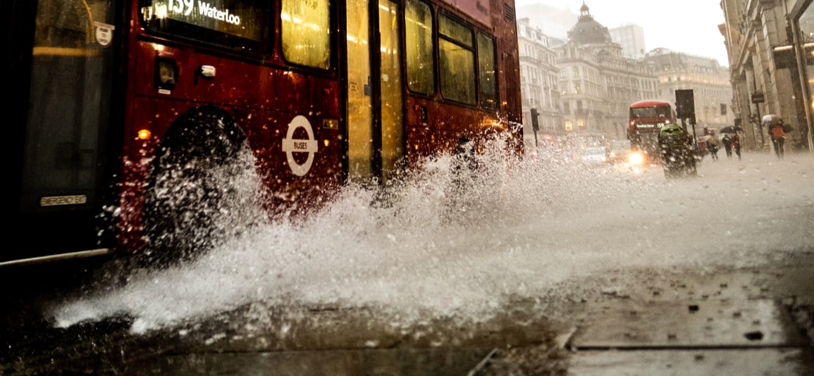 A wet London street scene with a bus splashing rain water on to the pavement in Regent Street