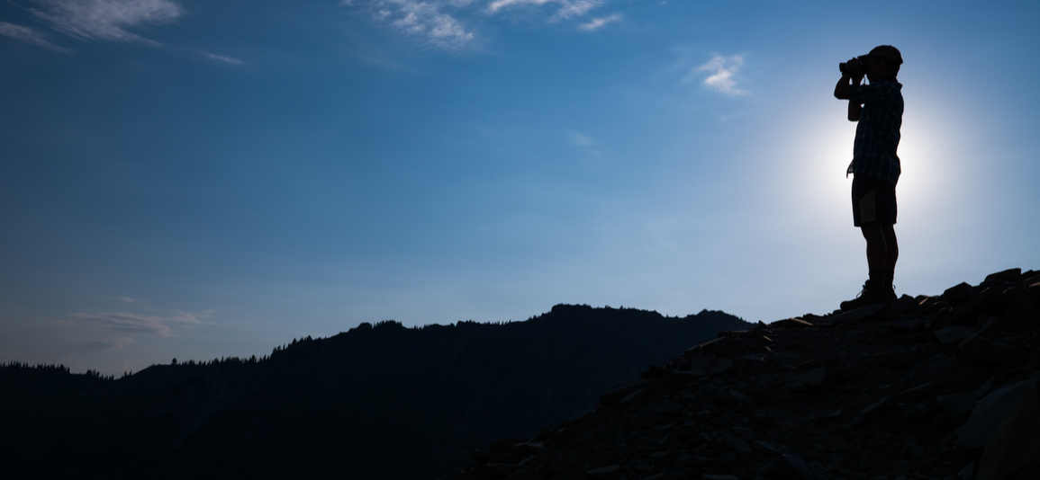 person looking over the horizon with binoculars