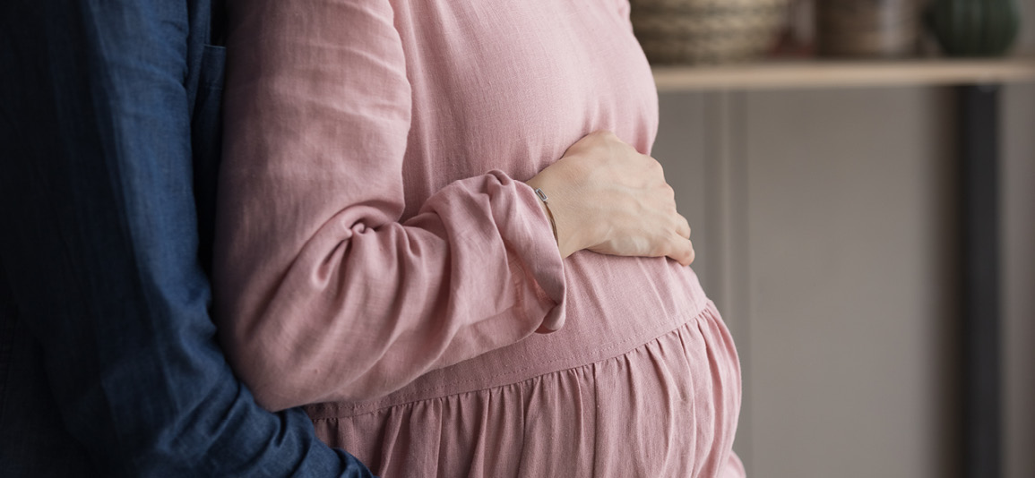 Loving young man and pregnant woman holding hands on belly