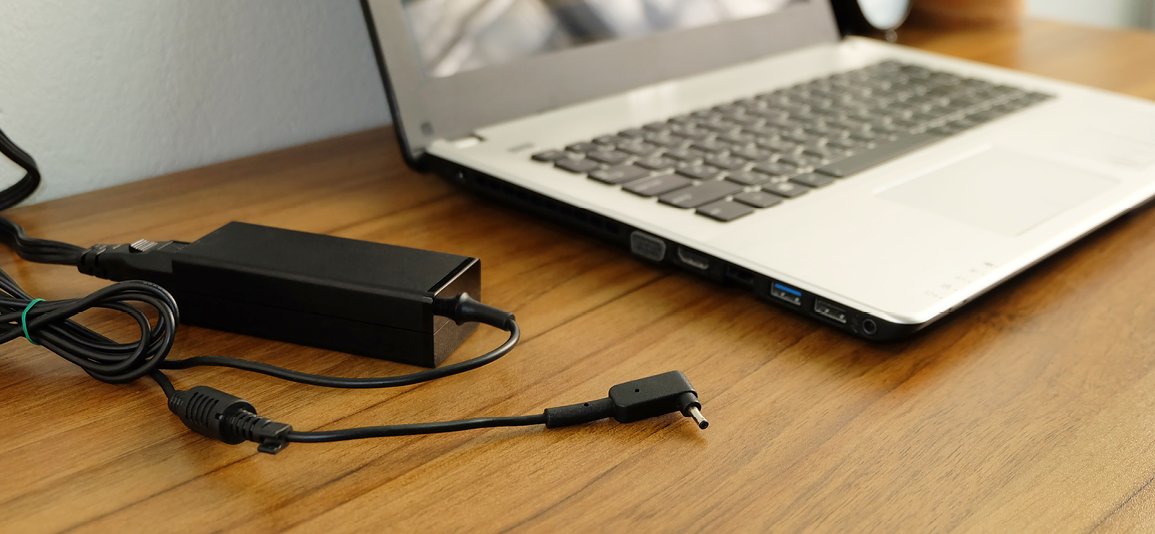 Plug in power outlet adapter cord charger on a white wall of the laptop computer on Wooden floor