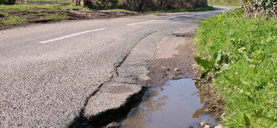 Unrepaired surface damage to tarmac on a rural road