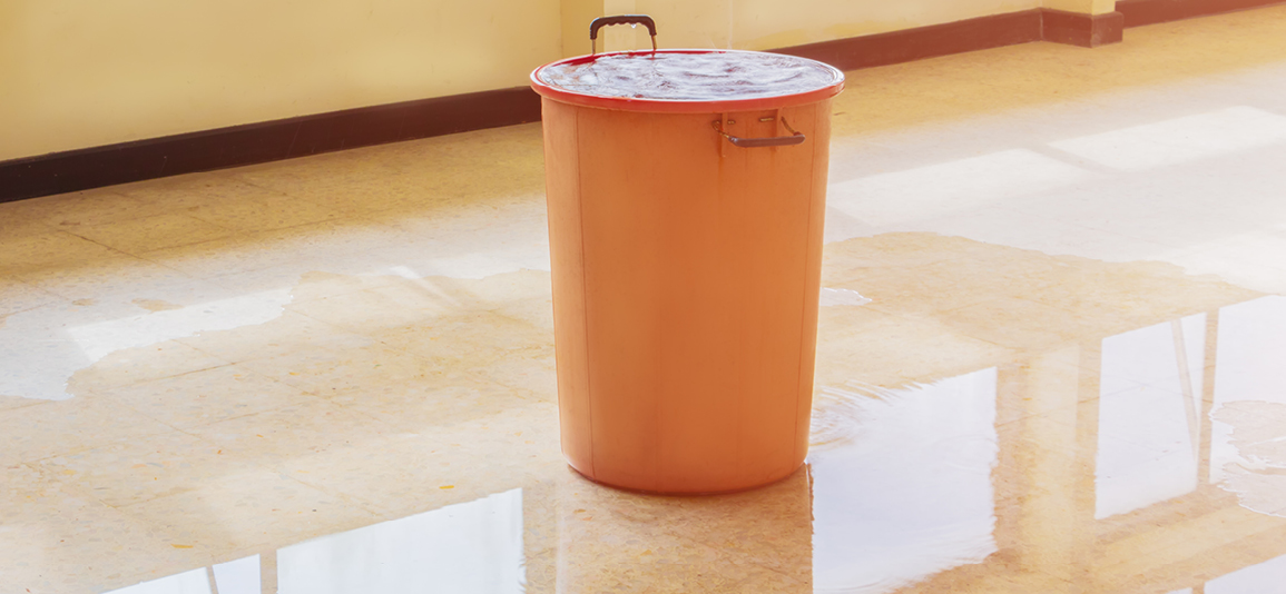 bucket full of water surrounded by a wet floor from a ceiling leak