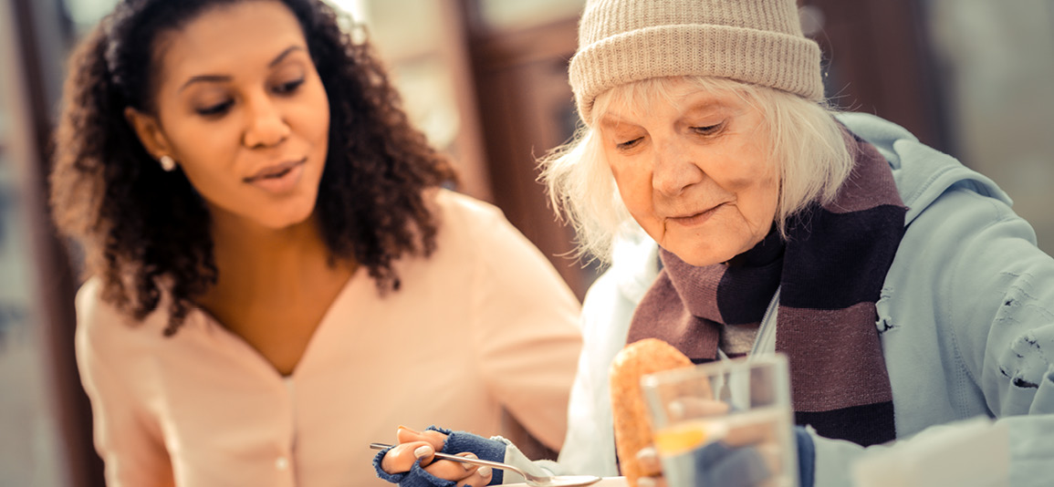 Volunteer keeping older person company white eating warm food