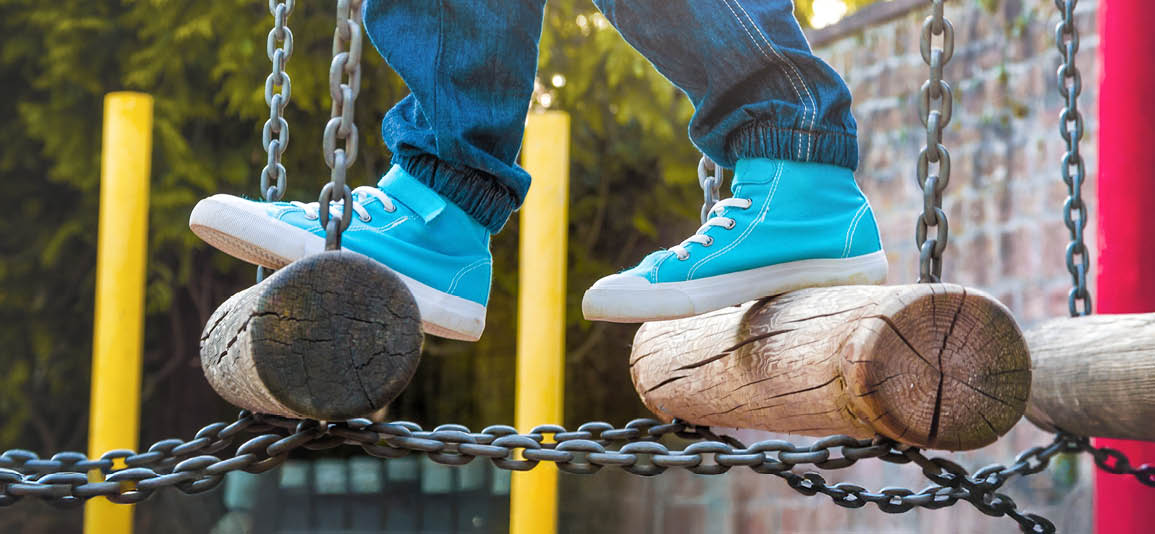 Close up of a child's feet wearing trainers walking across a playground obstacle bridge 