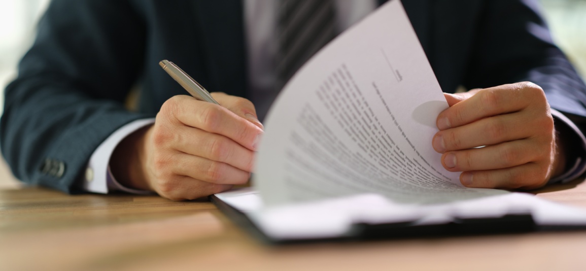Businessman leafing through documents and signing contract for business deal at work in office closeup