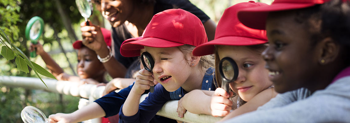 Kids and teacher with magnifying glasses outside