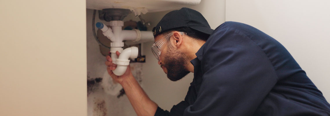 Plumber fixing leak by sink