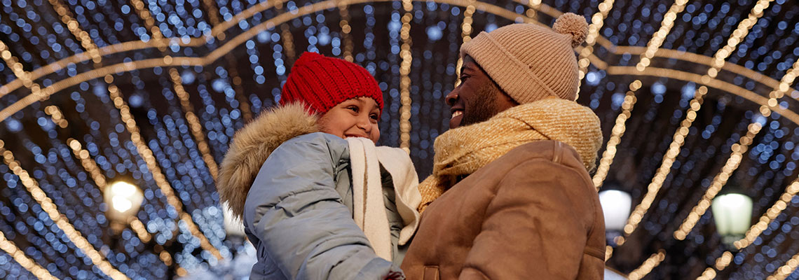 Father holding child under Christmas lights