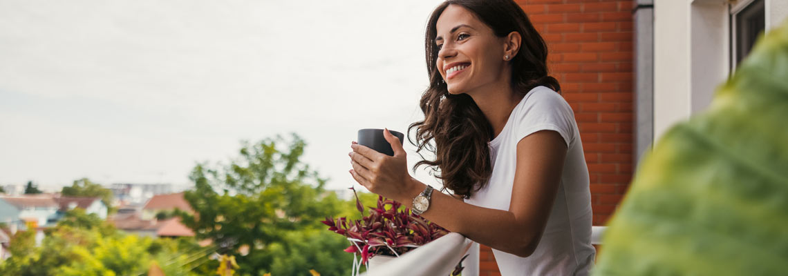 young woman relaxing over a cup of tea while standing on the balcony