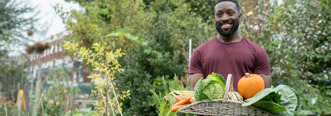 smiling man holding basket with fresh vegetables in urban garden
