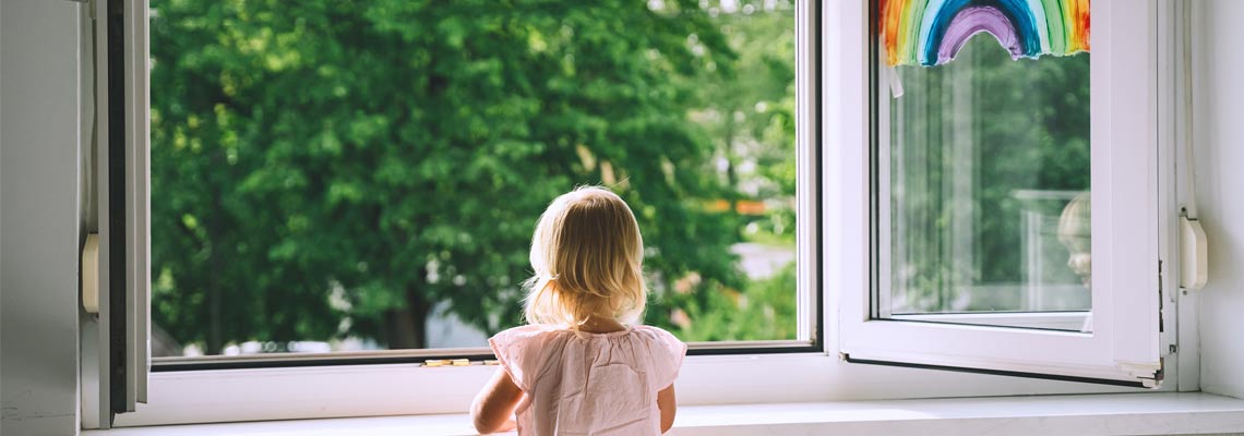 Little girl looks out open window at spring time