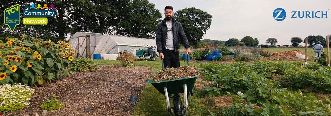 Man with a wheelbarrow in a garden with Zurich, TCV, and Community Network logos
