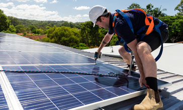 Solar panel technician with drill installing solar panels on roof